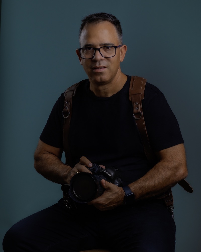 The photographer behind Sweetest Photos holding a camera against a teal background.