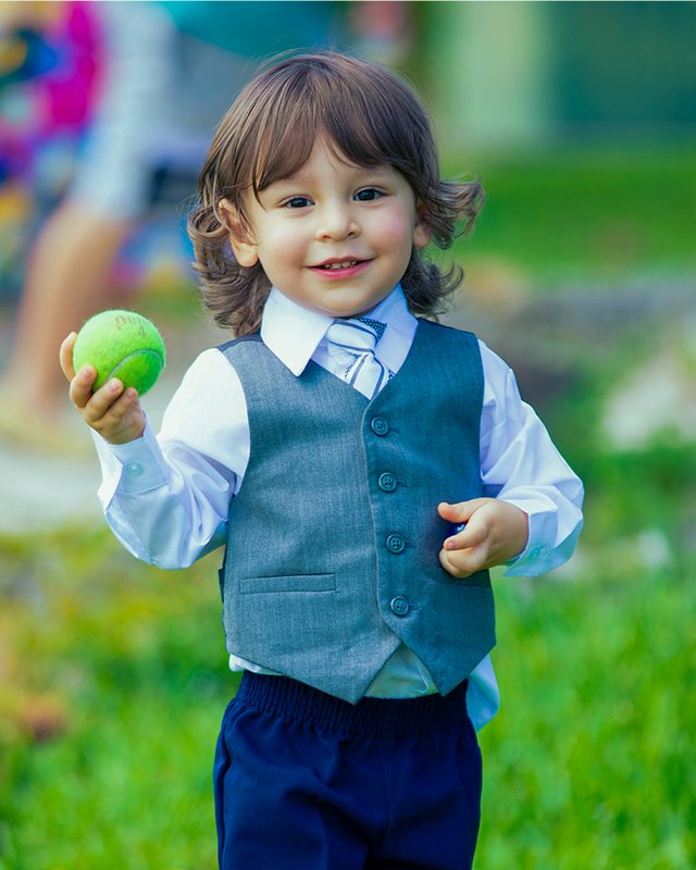 Child in a blue vest holding a green ball.