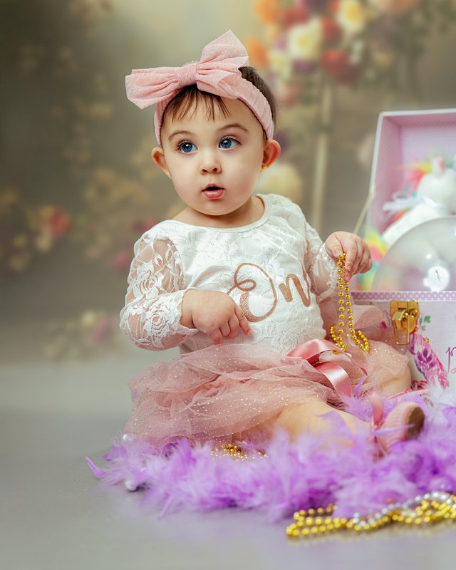 Baby with a pink bow seated among pastel decorations.
