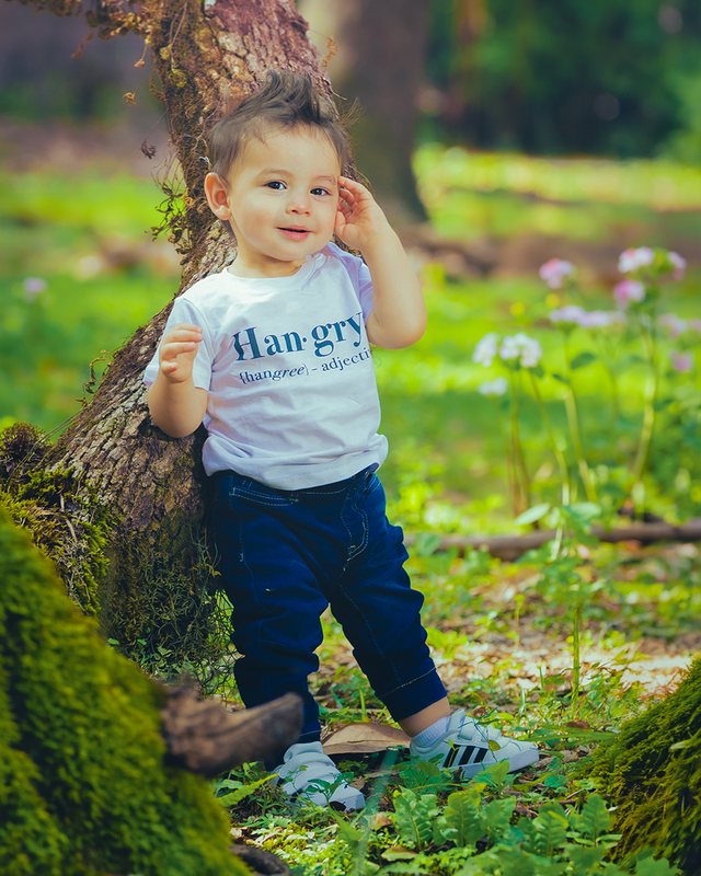 Young child standing beside a tree in a garden.