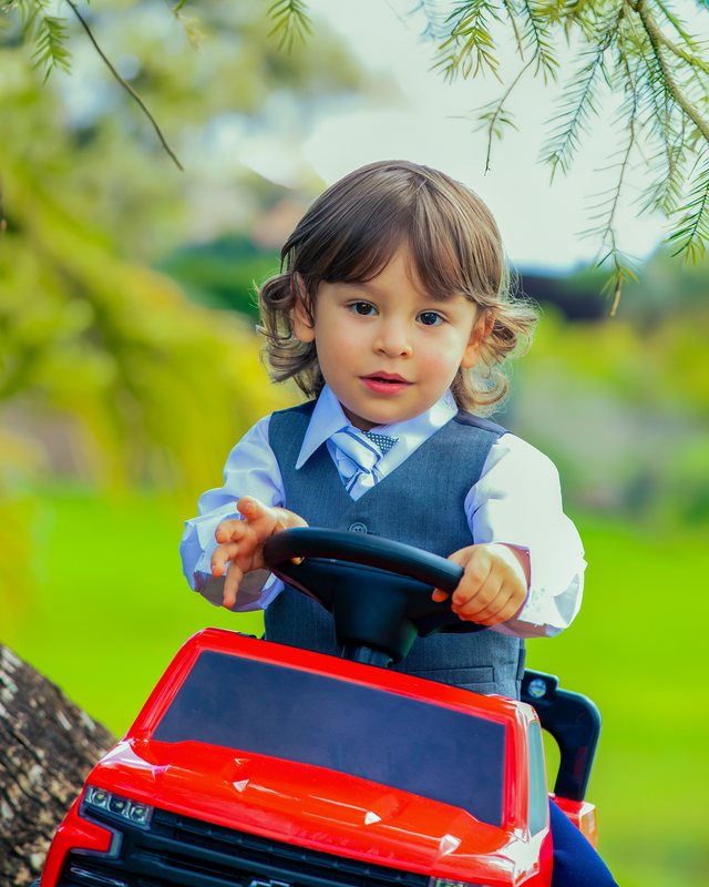 Child playing in a red toy car outdoors.