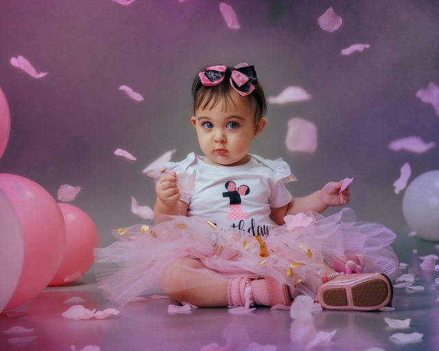 Baby in a pink birthday setting surrounded by decorations.