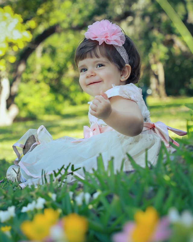 Baby wearing a pink flower headband seated on the grass.