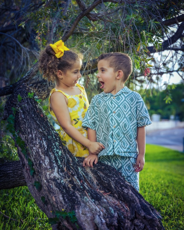 Two children smiling at each other while sitting on a tree branch.