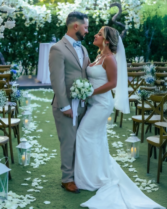 Bride and groom standing in a flower-lined outdoor aisle