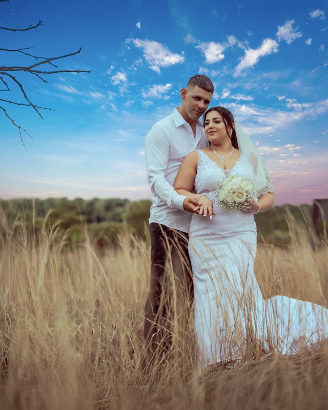 Bride and groom in a grassy field beneath a blue sky