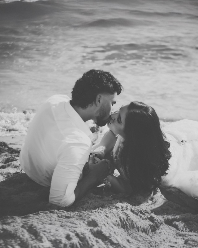 Black and white photograph of a groom kissing the bride beside the water