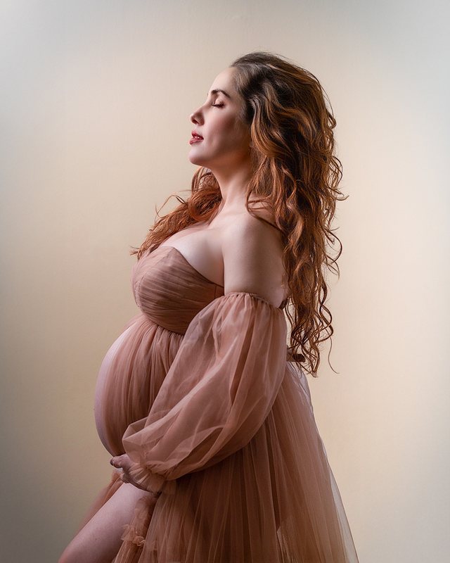 Expectant mother in a flowing rose-colored dress, photographed in profile.