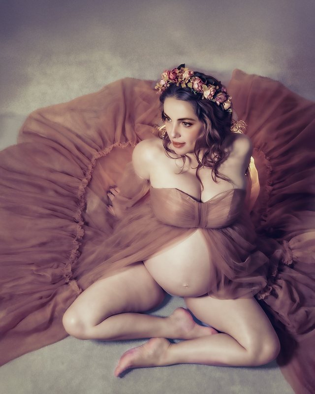 Expectant mother seated in a rose-colored gown with a floral crown.