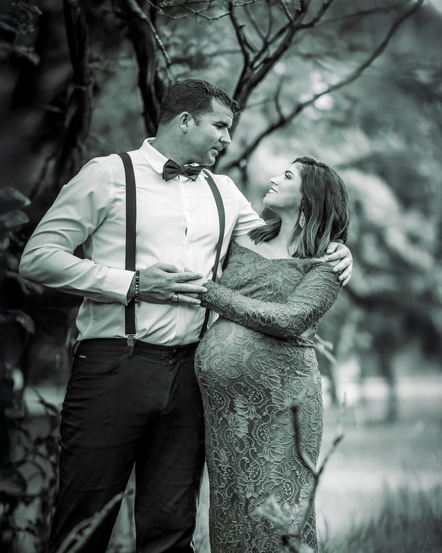Black-and-white maternity portrait of a couple beside a tree.