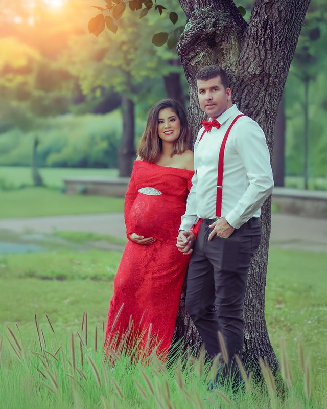 Couple outdoors with the expectant mother wearing a red dress.