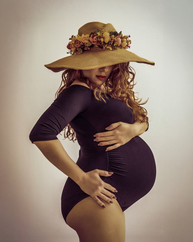 Maternity portrait in a black outfit and a wide-brimmed floral hat.