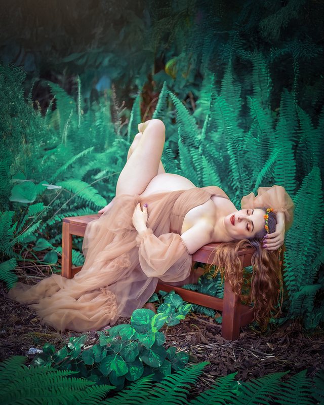 Expectant mother reclining on a bench surrounded by greenery.