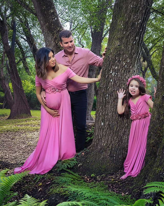 Expectant mother, partner and young girl in pink beside a tree.
