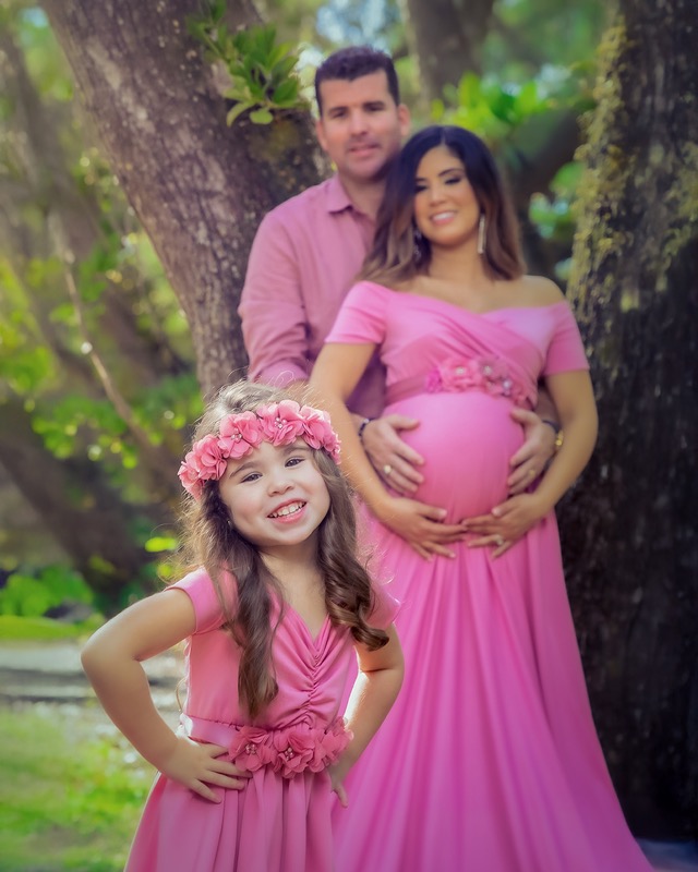 Smiling girl in pink in front of an expectant couple outdoors.